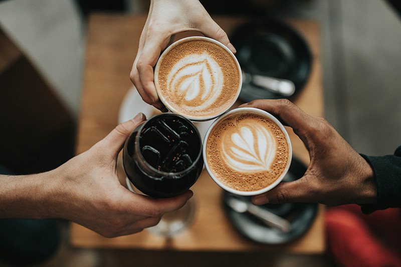 Blick von oben auf 3 Hände die schöne Kaffeegetränke halten